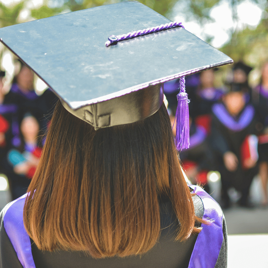 A girl in a black cap and gown faces a crowd during a graduation ceremony