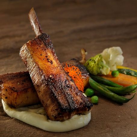 Roasted pork rib and belly with vegetables on stone.