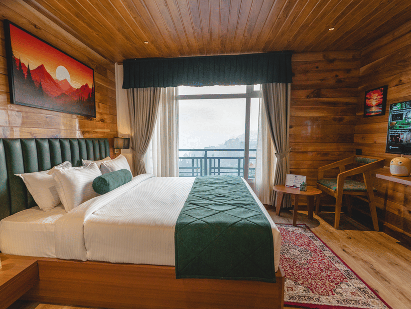 The bedroom of Presidential Suite with Bathtub featuring a double bed with a green bed runner, a wall-mounted television, a seating area and a balcony overlooking the town | Mount Lungta Boutique Hotel & Spa