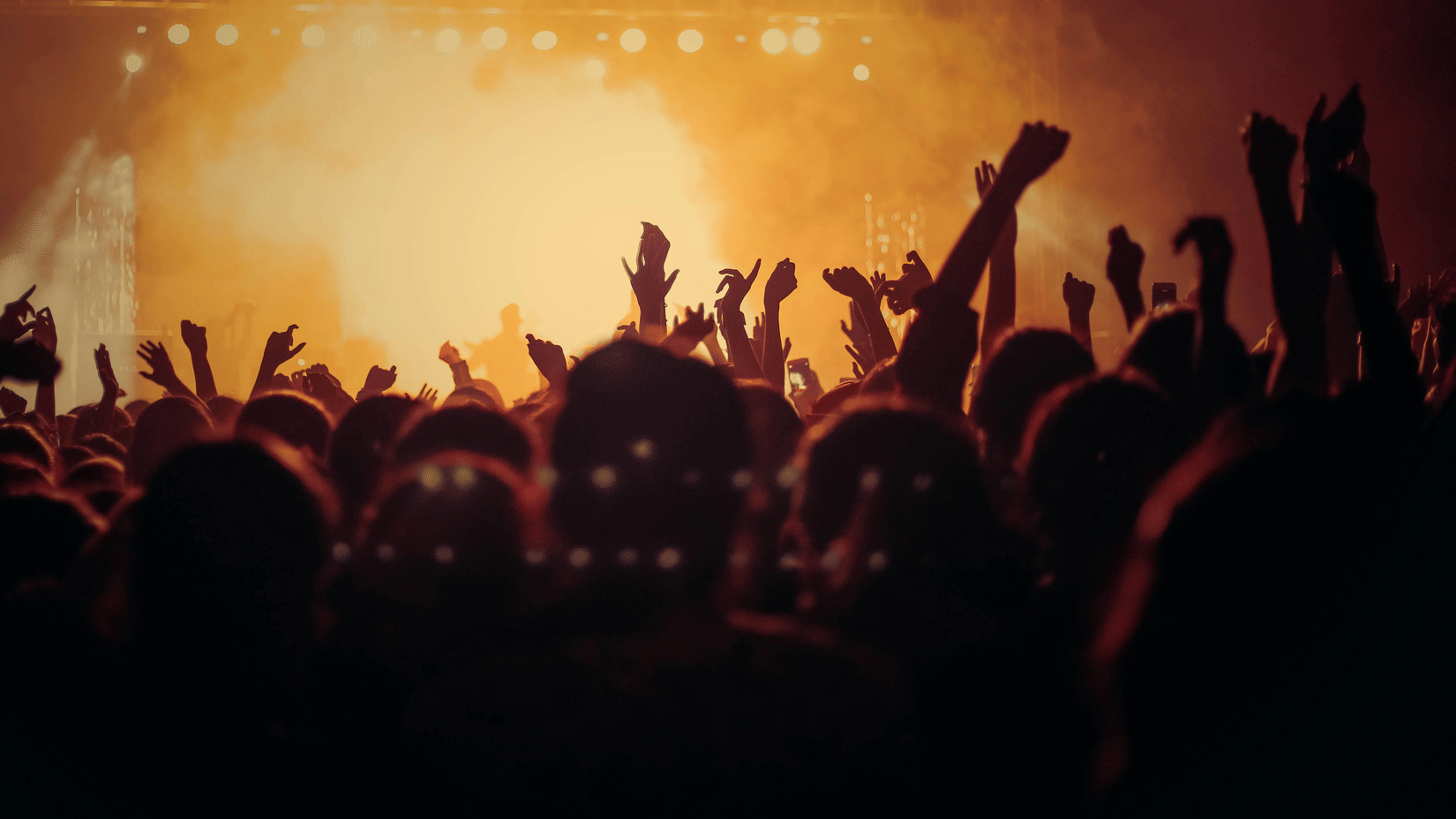 Festival crowd with raised hands enjoying a high-energy live music performance under bright stage lights