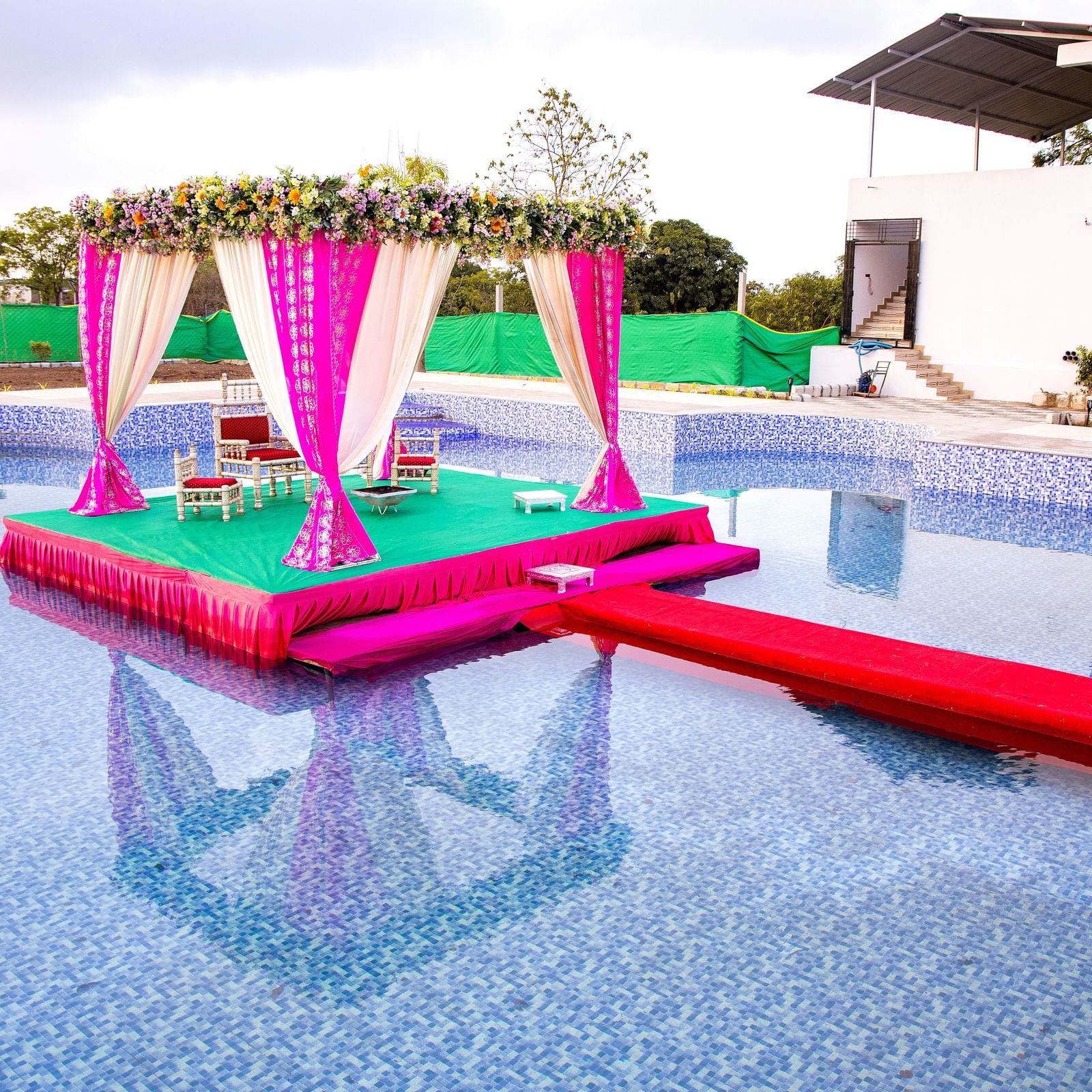 A customised podium placed between a pool half-filled with water and has an elevated walkway, showcasing a setup for an event at Daksh Eden Greenz, Sasan Gir.