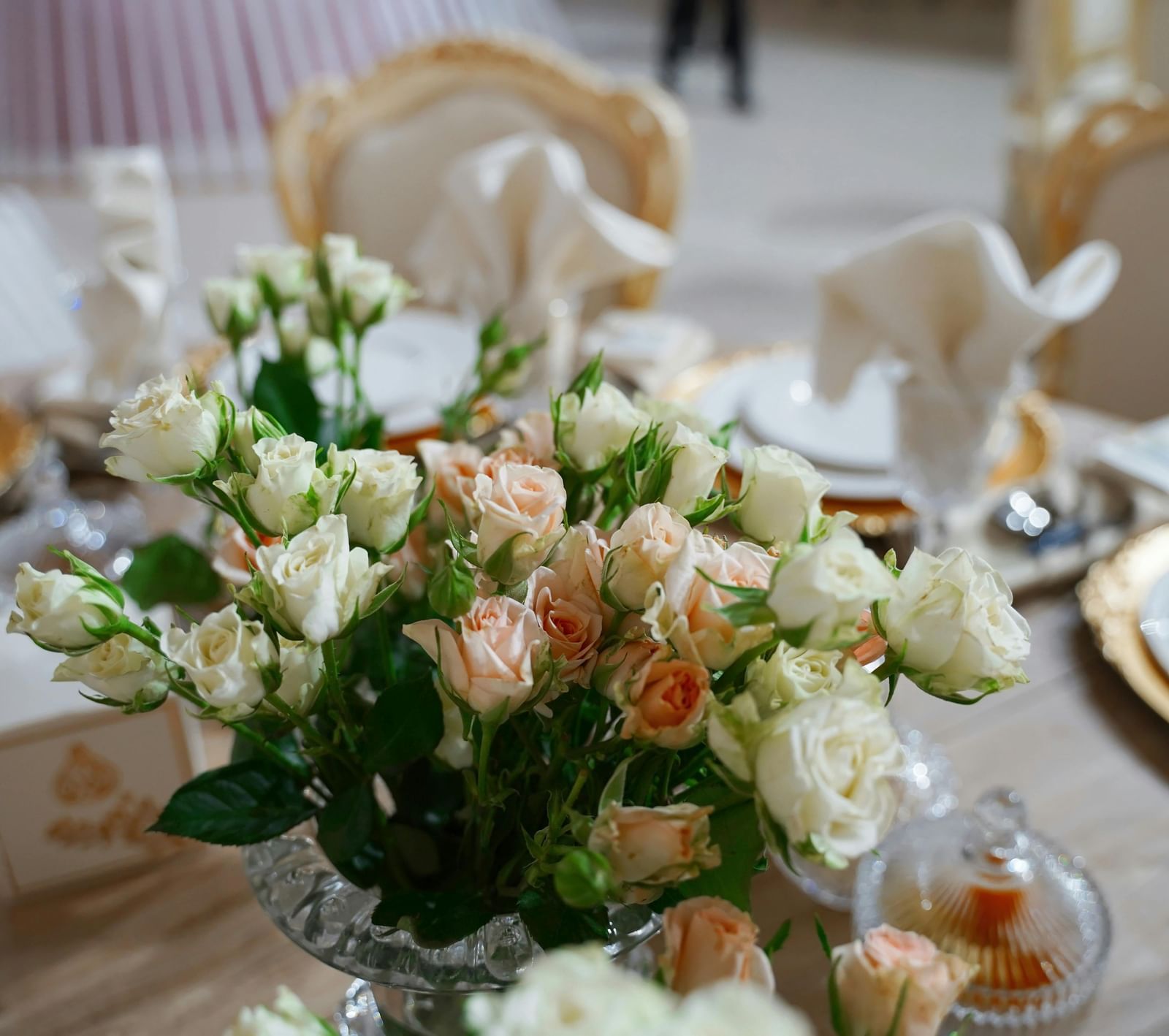 A close up shot of a beautiful flower vase with a lot of white and pink roses on a dining table.