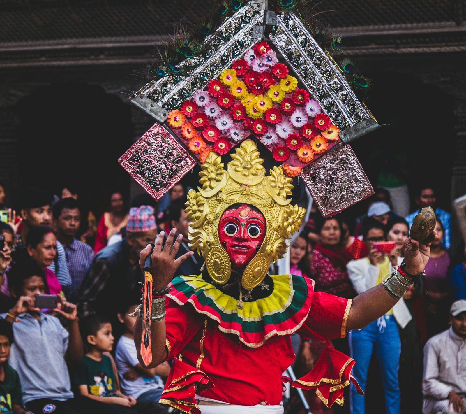 A person in a vibrant traditional costume and mask performing in front of a crowd.