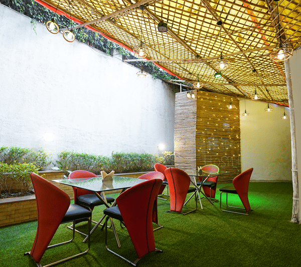 Outdoor terrace dining area with red chairs and glass-topped tables under a pergola.