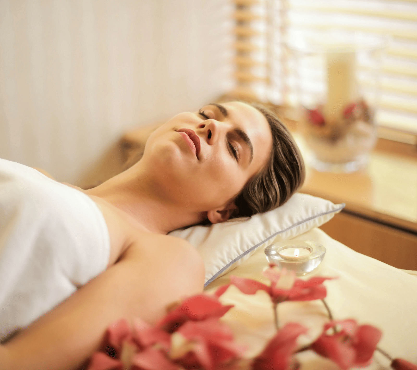 A woman lying down on a bed all relaxed in a brightly lit room.