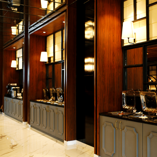 Buffet warmers with brass dome lids on dark wood cabinetry at Polo Hotel, Agartala under wall sconces and mirrored panel detailing.