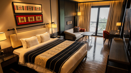 Spacious guest bedroom with double bed, seating area, writing desk, wall decorations, and large windows.
