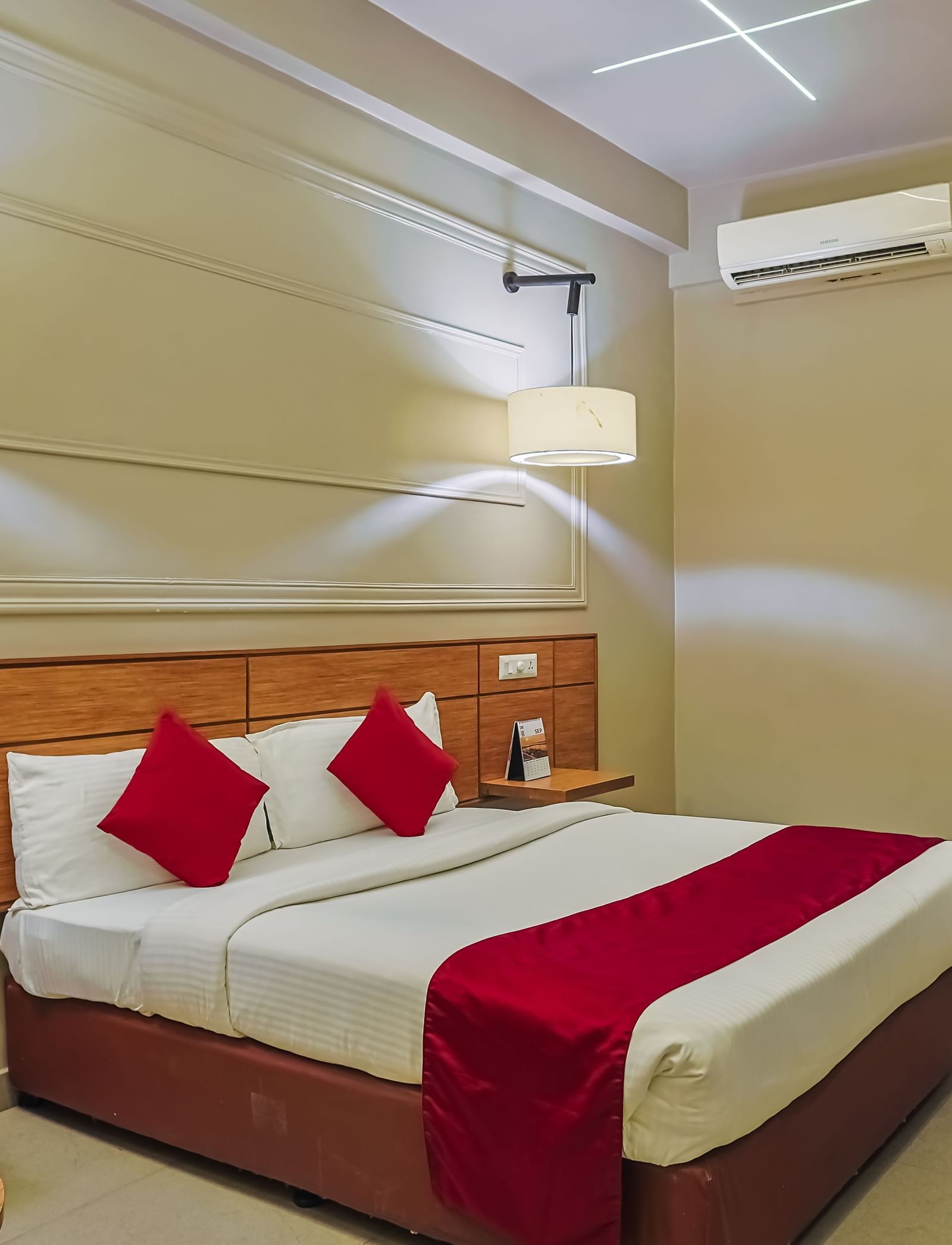 Bedroom with double bed, red runner, pillows, work desk and chair at Max Hotel Prayagraj.