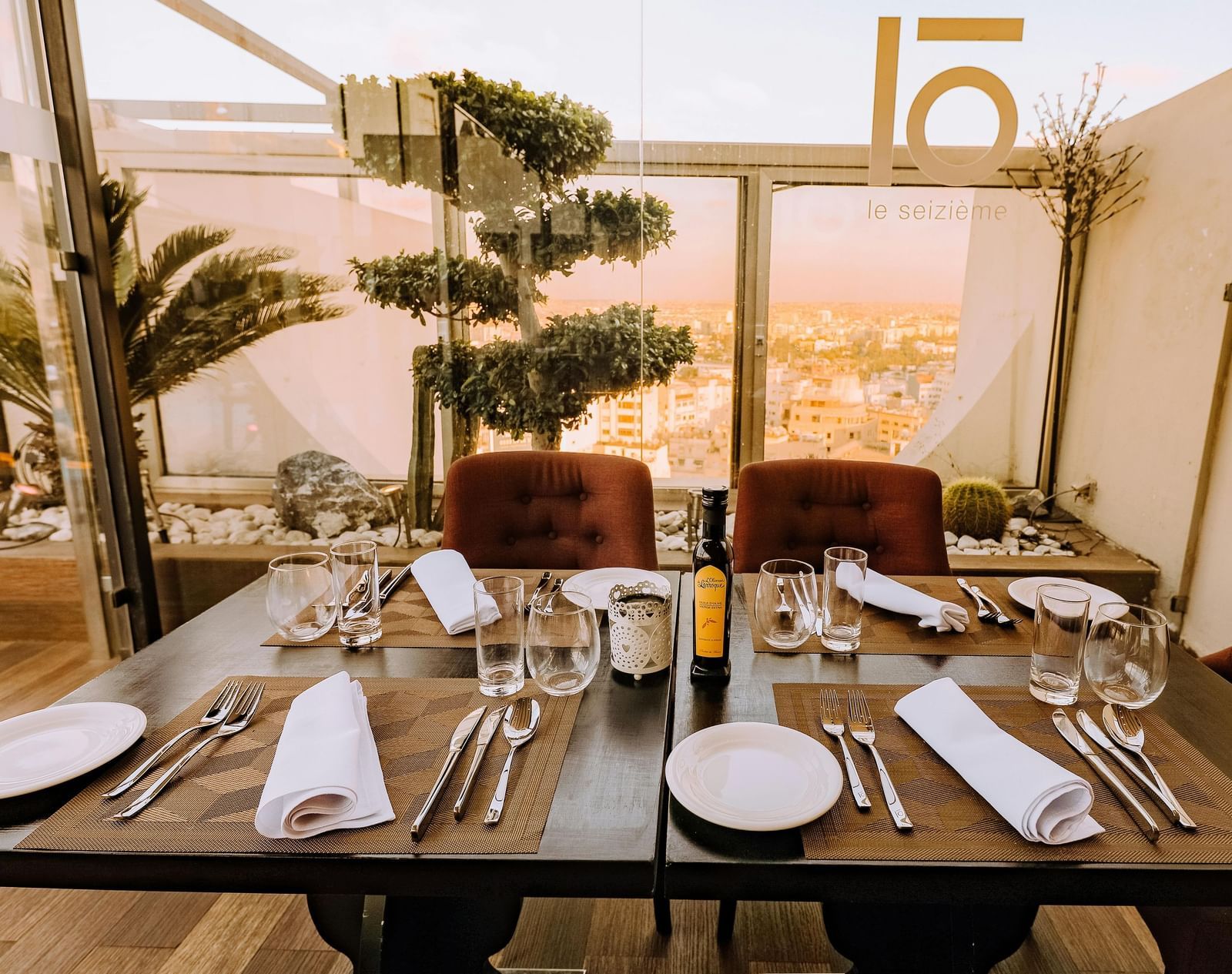A well-arranged dining table with cutlery and glassware featuring mesmerising city views in the background beyond the glass panels on the terrace.
