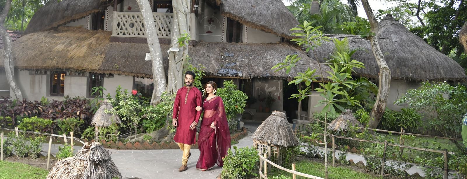 A traditional-style hut with a thatched roof, surrounded by lush greenery and a pathway leading to it | Bhoomi Restaurant