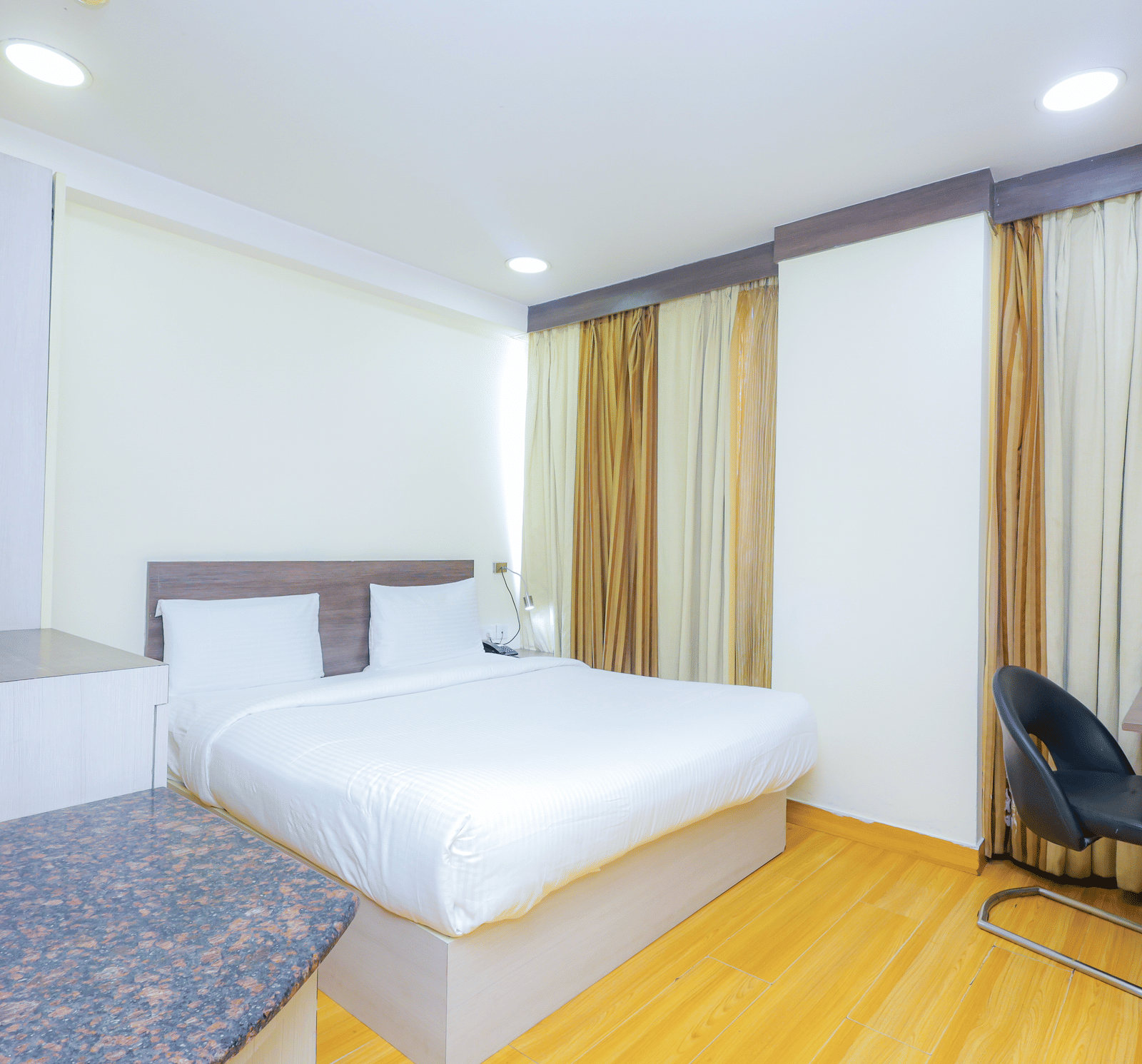 A bright hotel room featuring a bed, a desk, and large windows with privacy curtains - Hyphen Business Hotel, Noida
