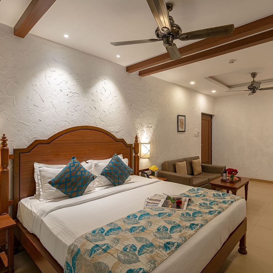 A hotel room featuring a neatly made and decorated bed, two wall-mounted lamps, a sofa, a side drawer, and a vanity.