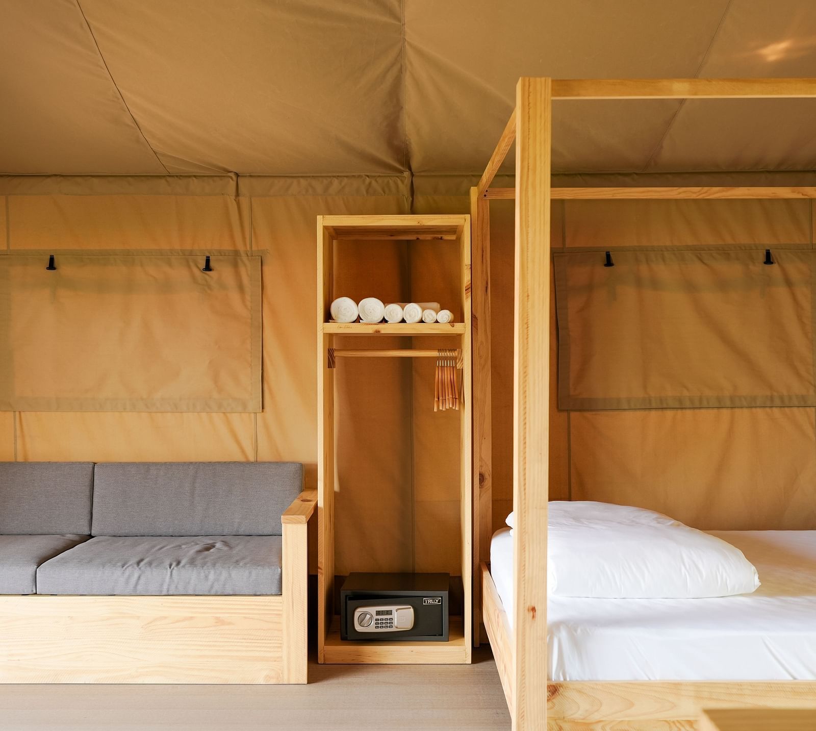 A thoughtfully designed interior of the Mindful Tent at WoCAL Retreat Ke Ga, showcasing a comfortable sofa and a neatly arranged bed with wooden dividers and shelves for storage.