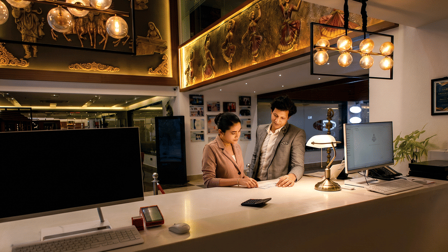  Reception team at the front desk with a banker's lamp and computer monitors below a gilded mural of dancers at Ilara Hotels & Spa, Tada.