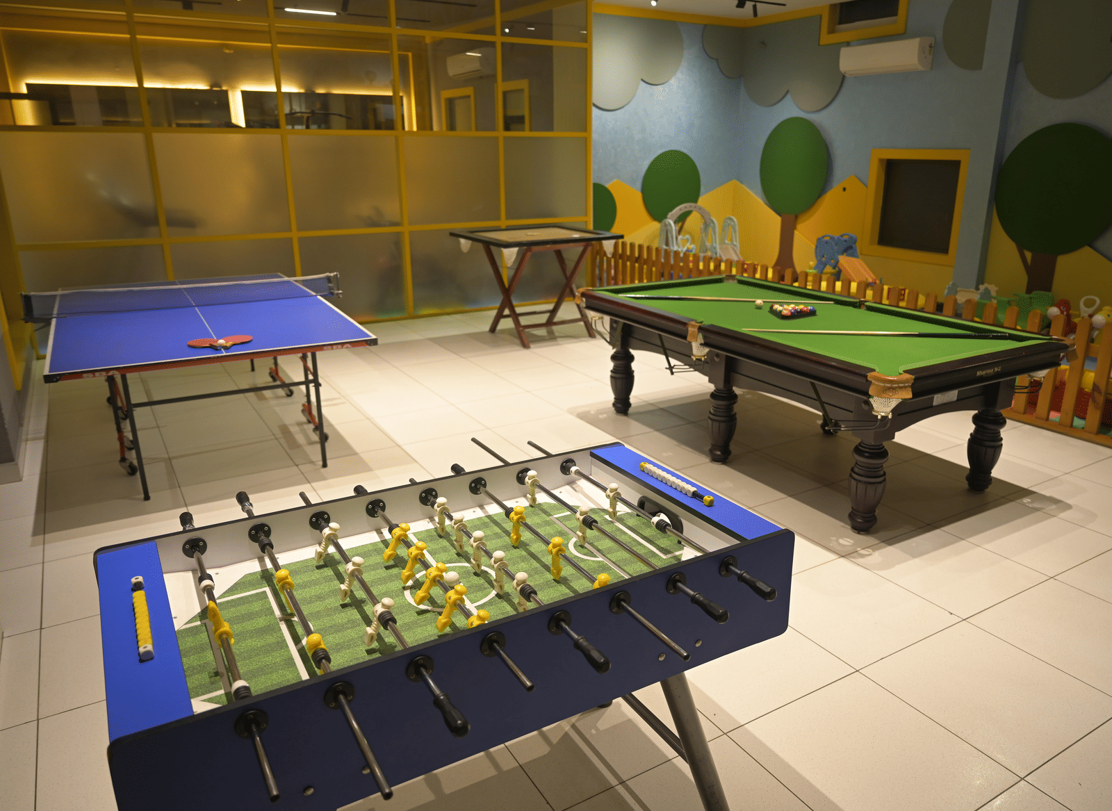 A bright indoor games room featuring a foosball table, a pool table, and a table tennis setup at Hotel Sonar Bangla Mayapur.