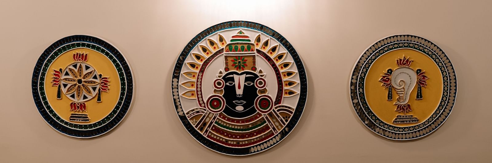Three decorative plates hanging on a light-coloured wall, illuminated by a warm light from above.