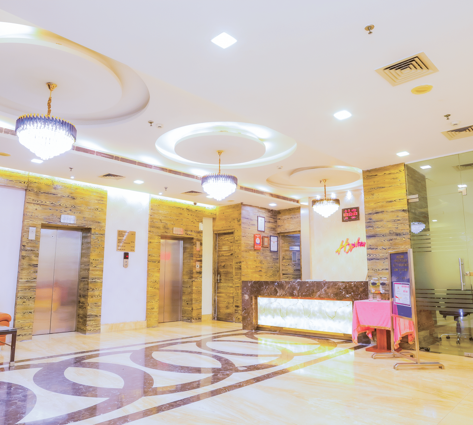 A brightly lit and elegant hotel lobby with a decorative floor, a reception desk in the background, and comfortable seating areas.