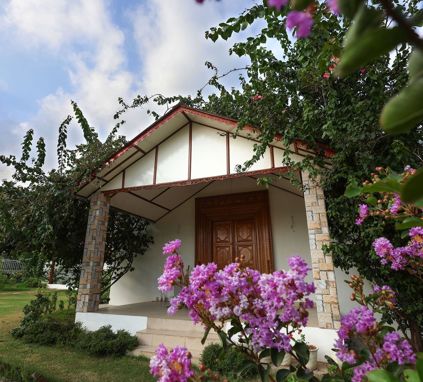 A charming cottage entrance with stone pillars and blooming purple flowers - Neer Ganga Resorts