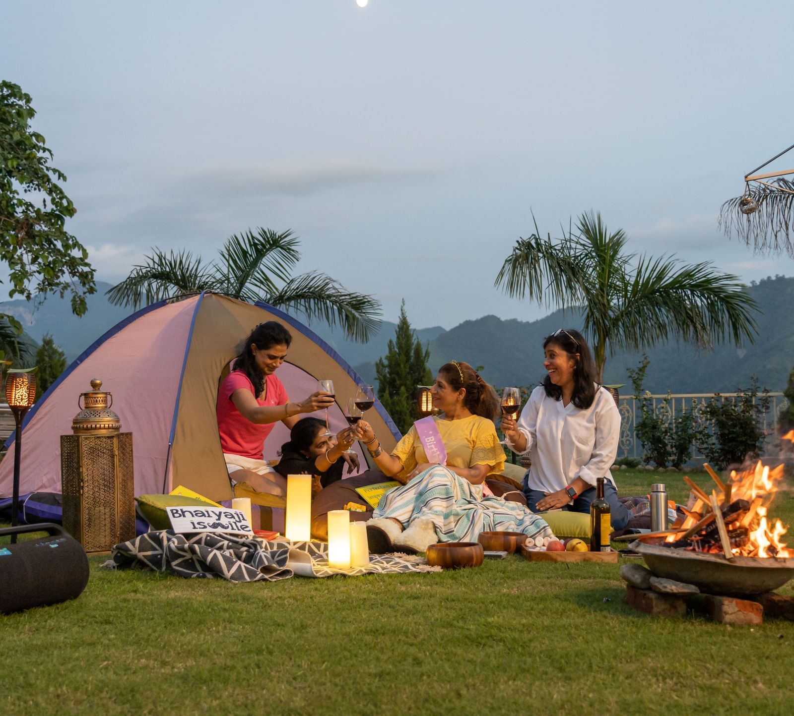 a group of women tenting on a garden area with a bonfire next to them - neer ganga resorts