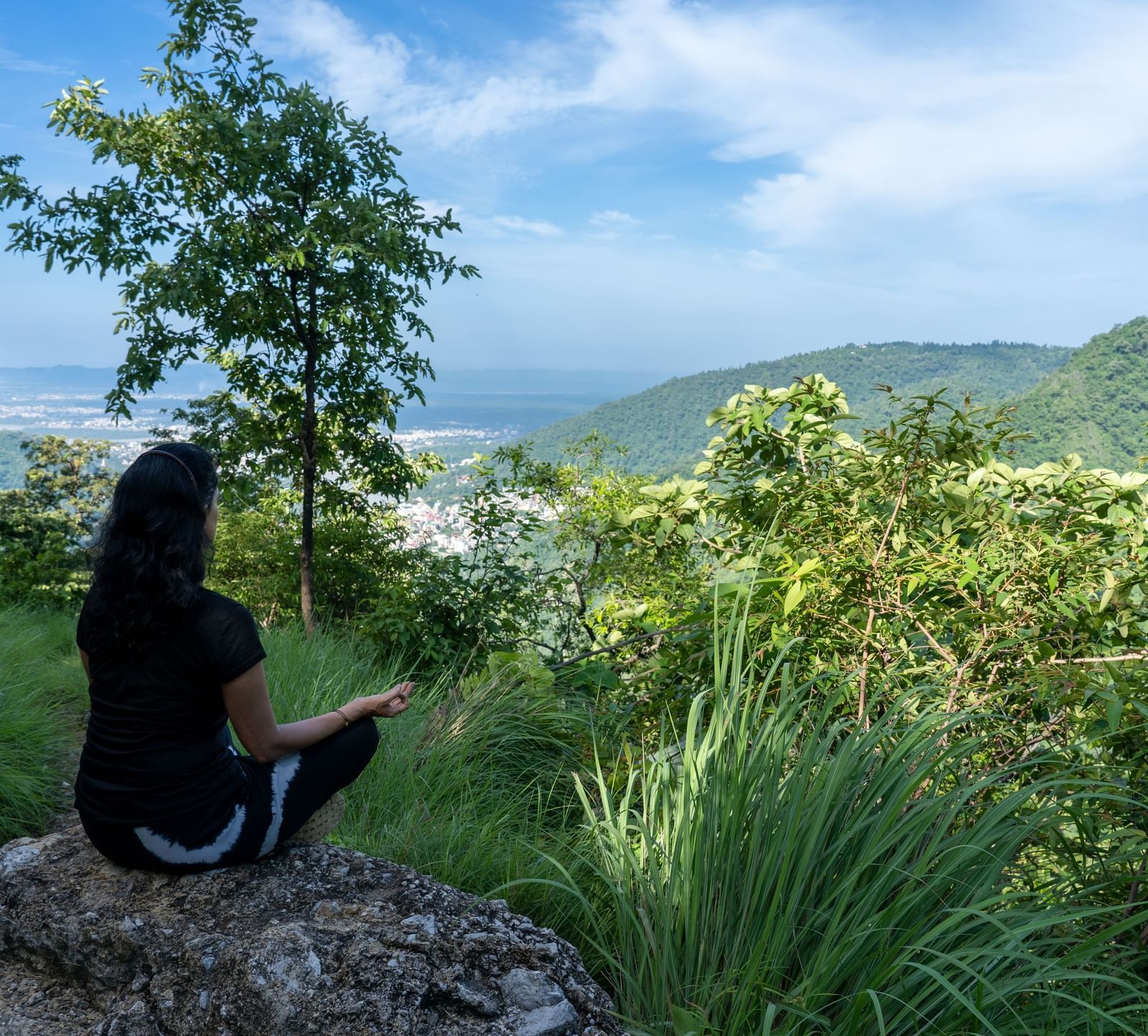 A lady meditating on the mountains sitting on top of a rock.