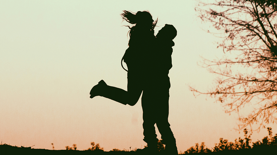 A romantic silhouette of a couple embracing against a sunset backdrop.