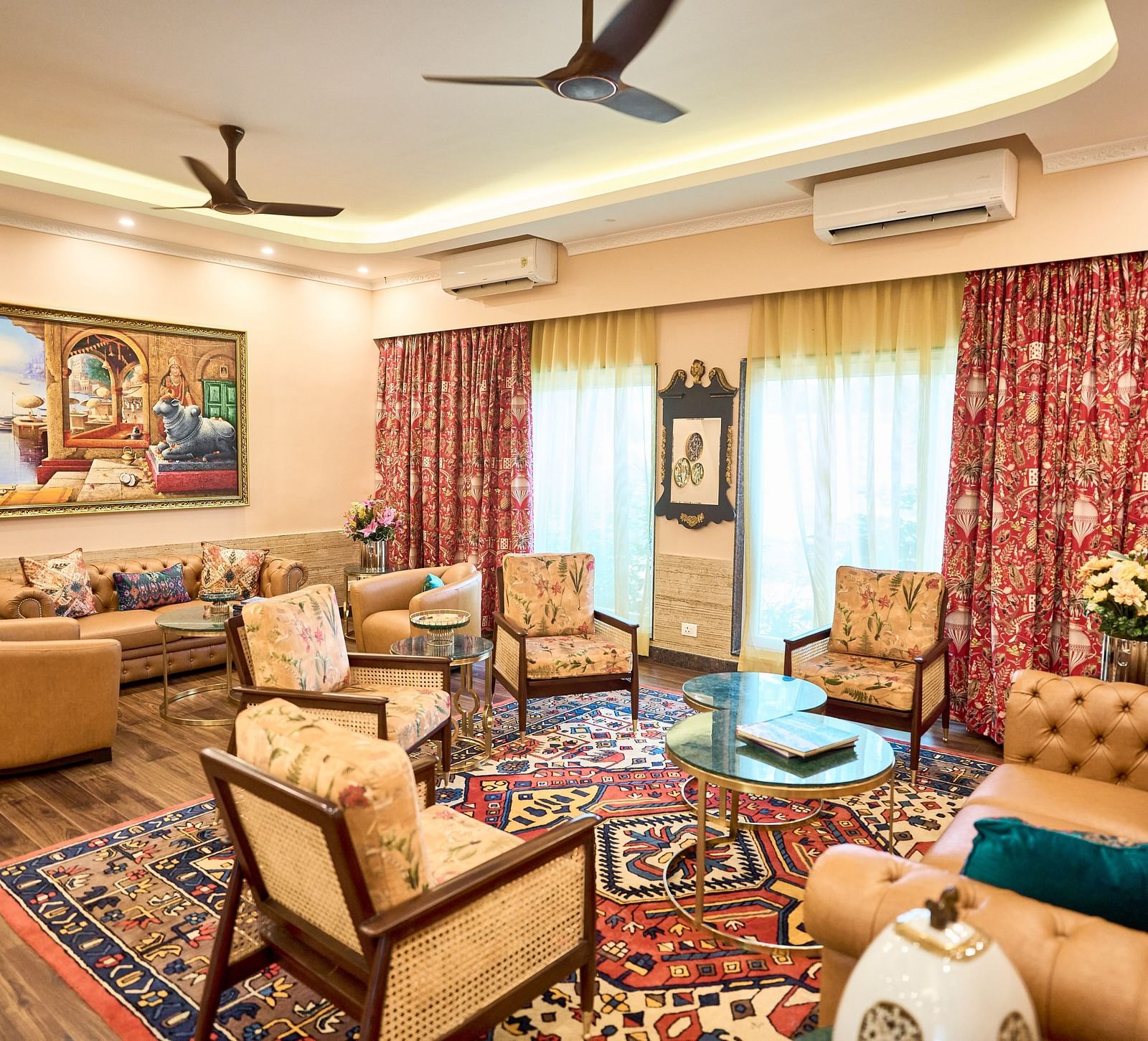  A seating area with plush furniture arranged around the table, curtains drawn to the side, and a wall-mounted painting at Mayfair Manor, Alibag