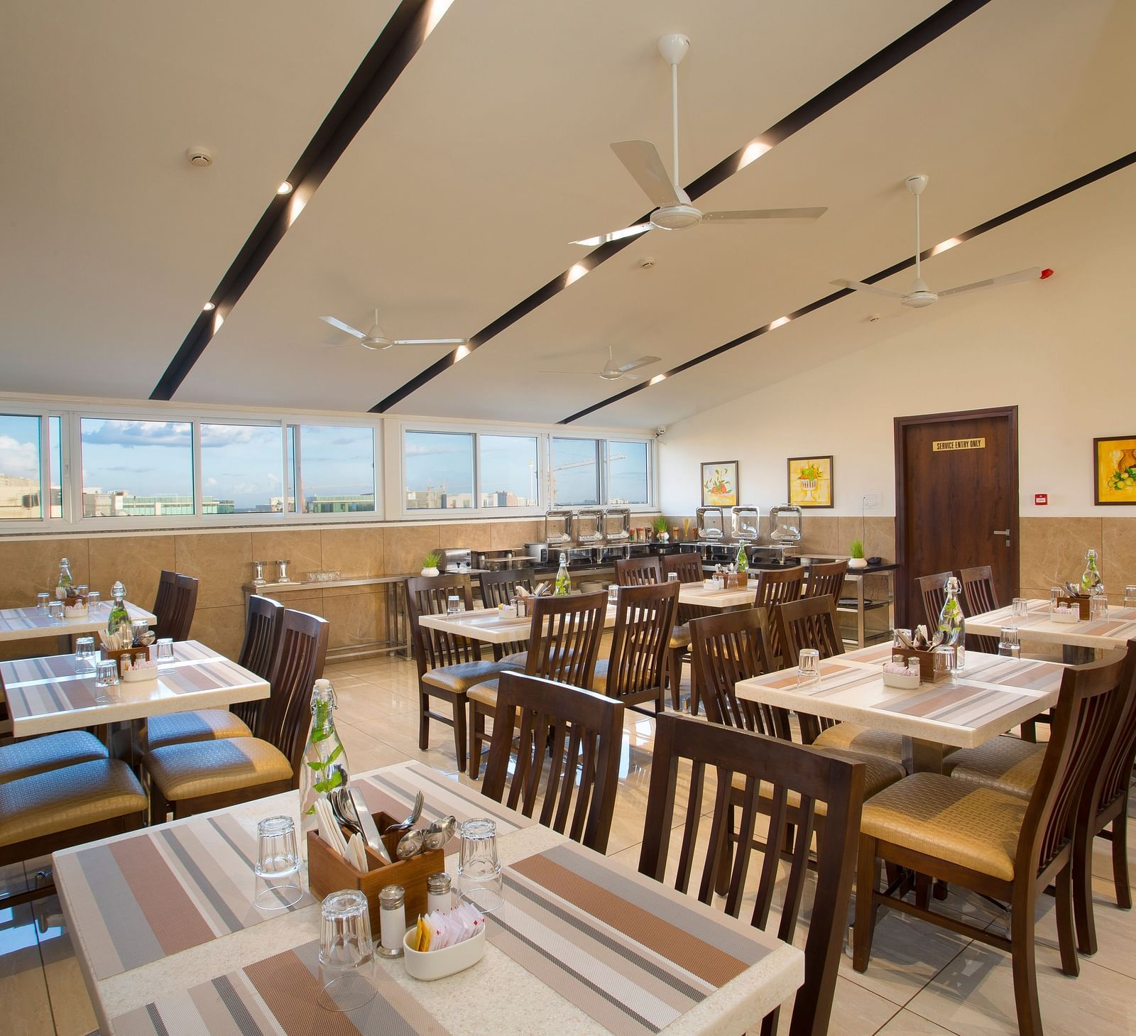 A hotel restaurant with wooden tables and chairs, large windows and ceiling fans - De Venetian by TGI, Brookefield