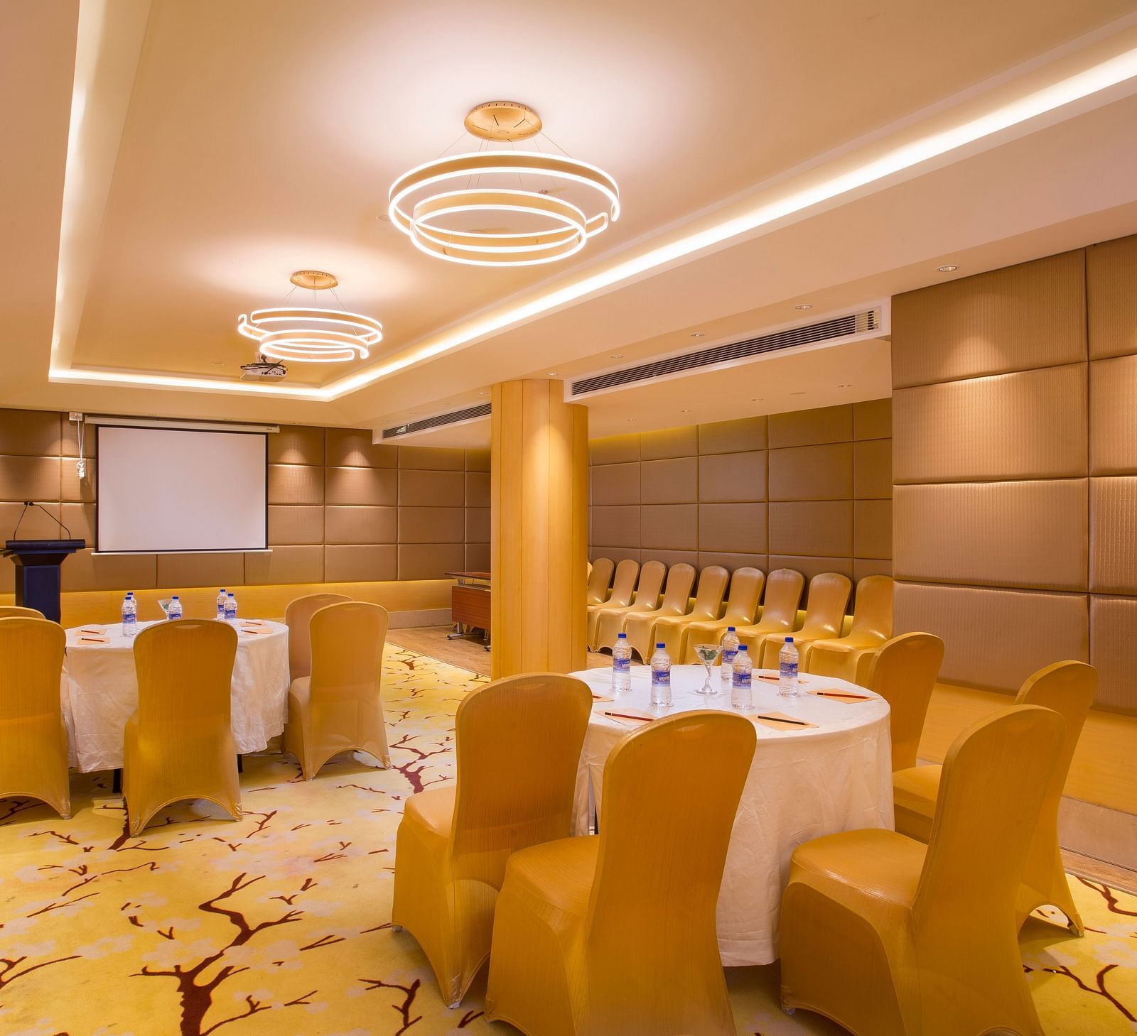 a conference hall with clusters of tables and chairs spread across the hall, where all the chairs are facing the projector - Hotel Fountain Tree By TGI - JP Nagar, Bangalore