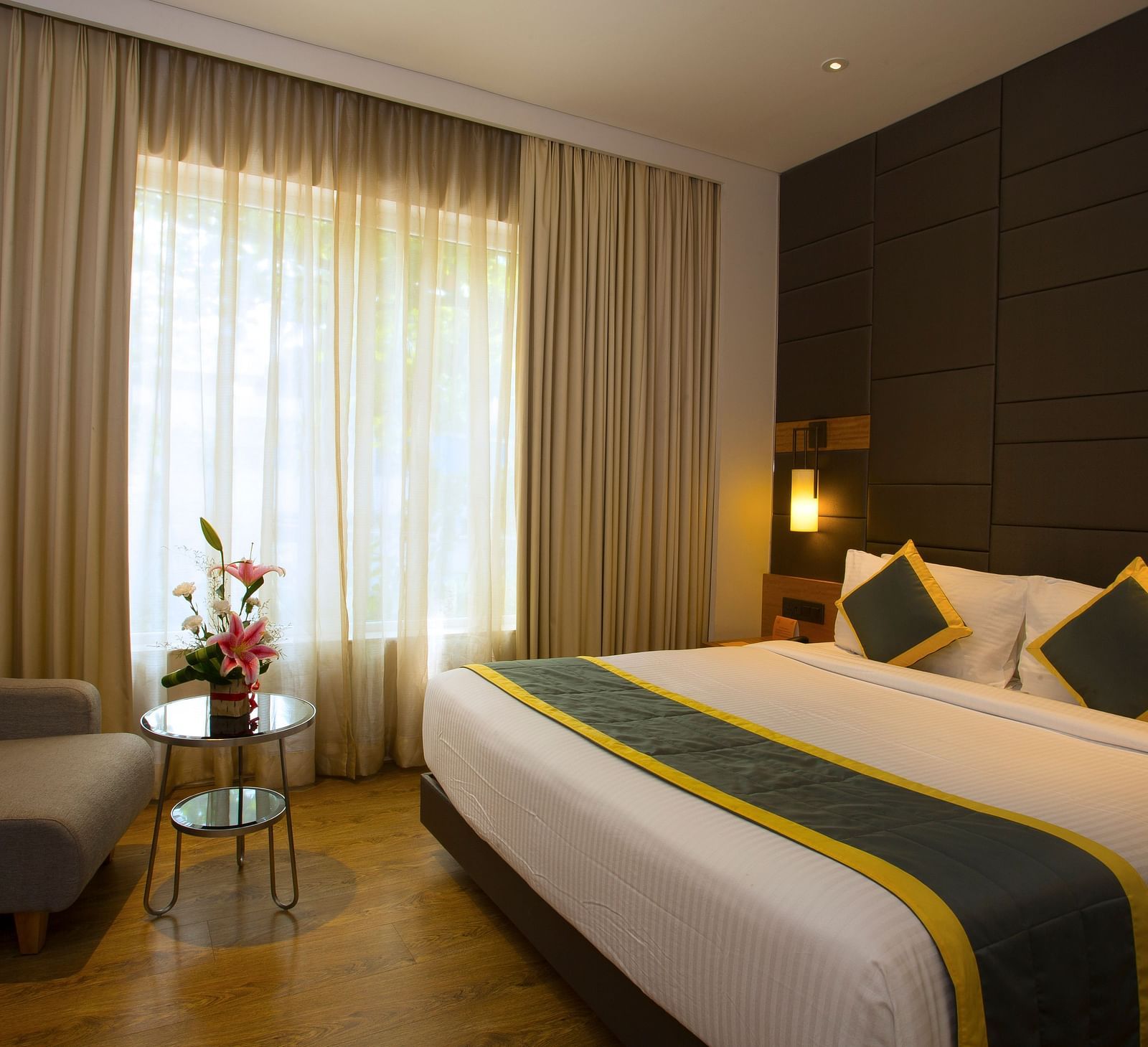 a bedroom with a large bed and a sofa opposite the the bed, with a small table in the middle - Hotel Fountain Tree By TGI - JP Nagar, Bangalore