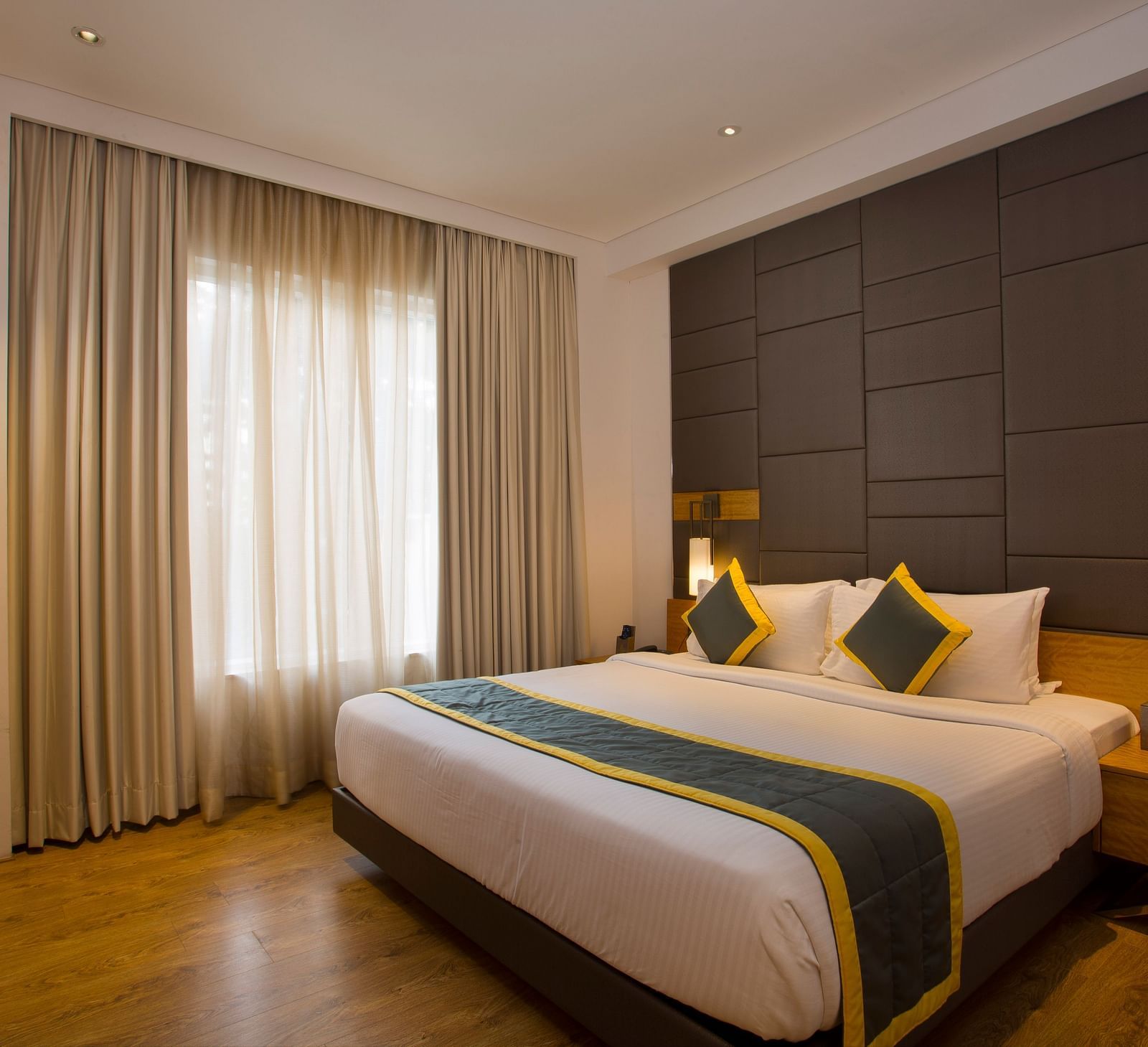 a bedroom with a large bed opposite a television mounted on the wall and side drawers on each side - Hotel Fountain Tree By TGI - JP Nagar, Bangalore