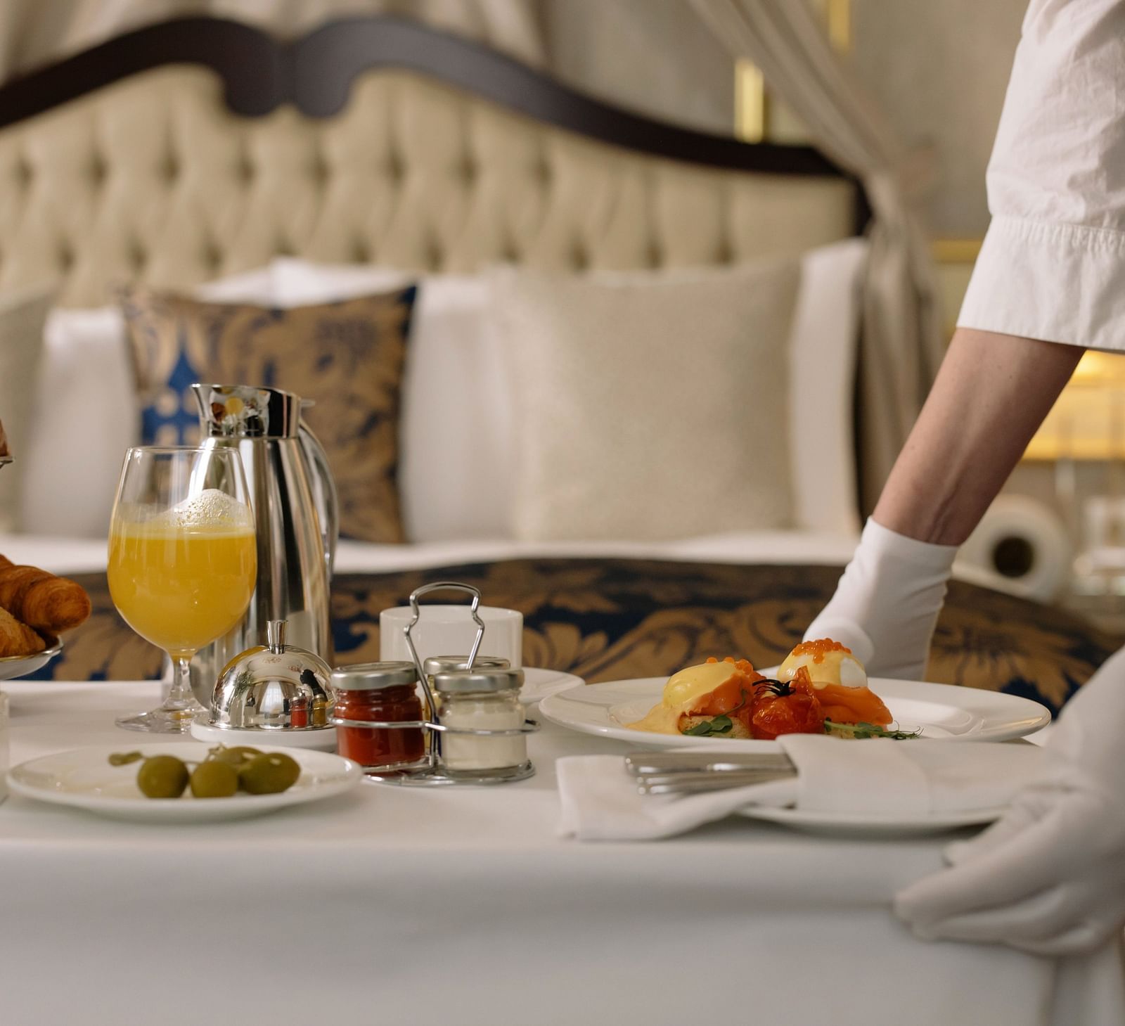 A room service attendant serving breakfast with eggs and pastries on a bed