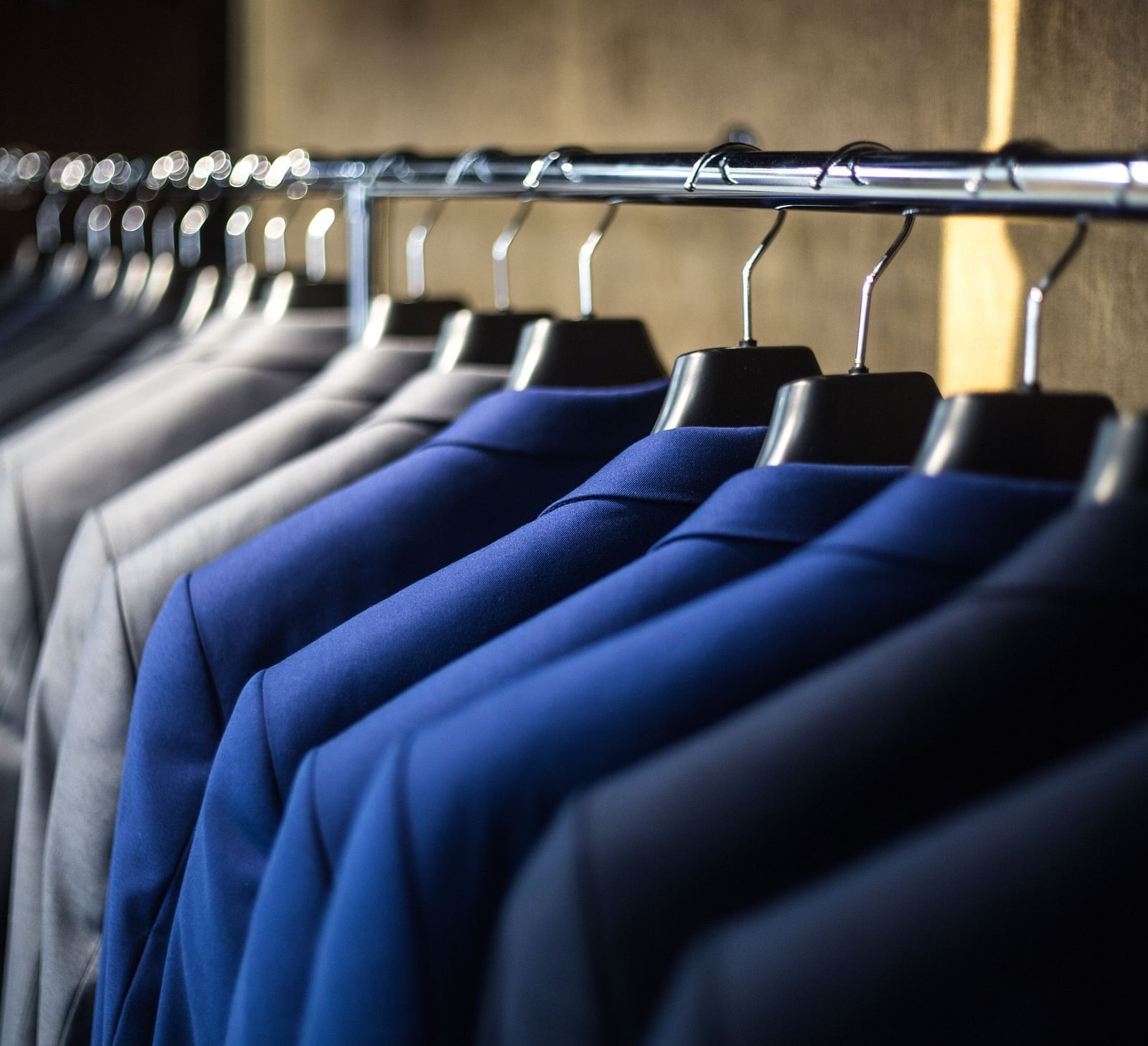A selection of blue and grey suits on hangers in a closet