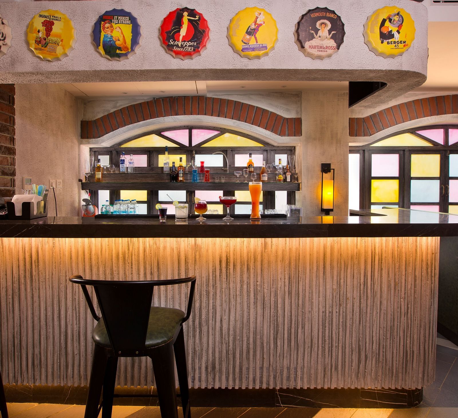 A stylish bar with colourful stained glass windows, a variety of drinks on display and vintage advertisements on the wall - Hotel Southend by TGI - Bommasandra, Bangalore