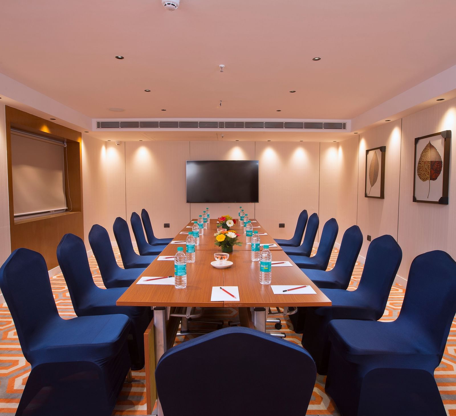A well-lit boardroom with a long table, blue chairs and a large screen on the wall, suitable for business meetings - Hotel Southend by TGI - Bommasandra, Bangalore