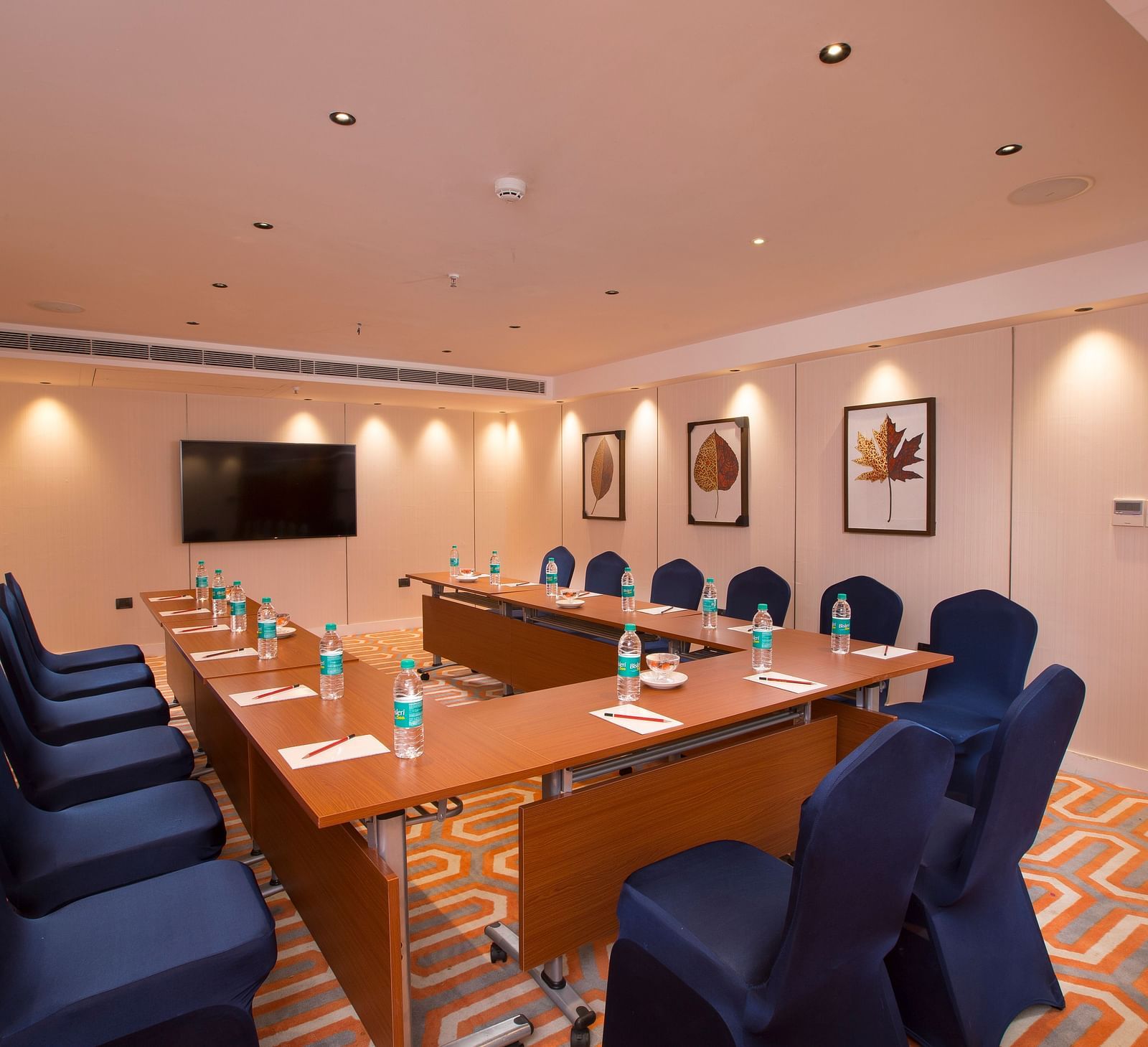 A formal boardroom with blue chairs around a long table, a flat-screen TV on the wall and framed leaf prints - Hotel Southend by TGI - Bommasandra, Bangalore