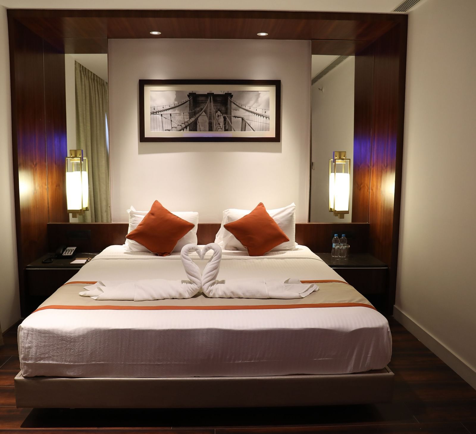 The front view of a hotel room with a large bed, white linens, burnt orange accents and a framed picture of a bridge above the headboard - Hotel Southend by TGI - Bommasandra, Bangalore
