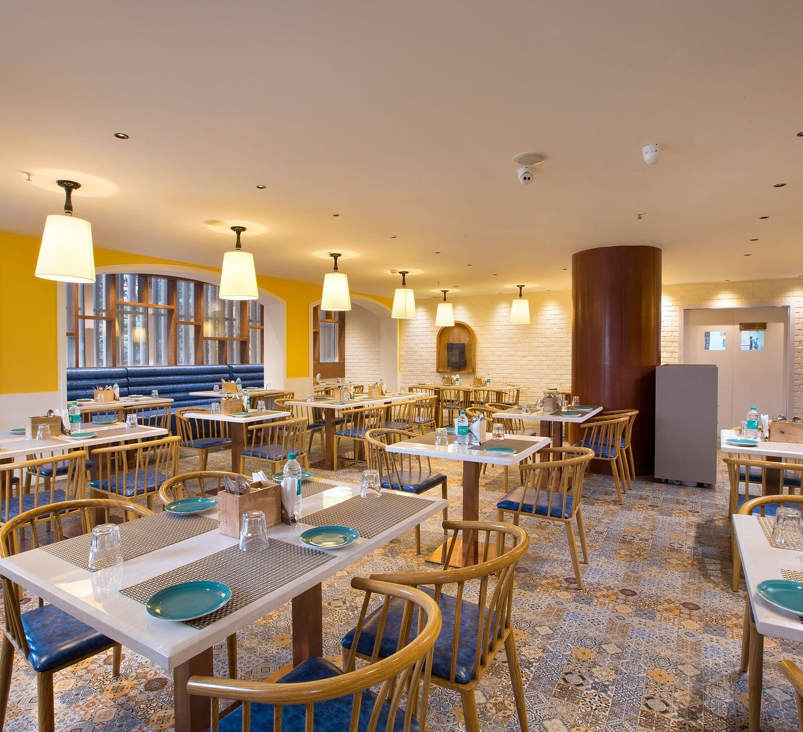 Another view of a spacious and brightly lit restaurant with wooden chairs, patterned tile floor and large windows - Hotel Southend by TGI - Bommasandra, Bangalore