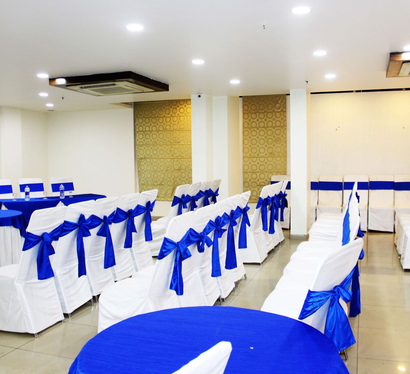 A banquet hall with chairs tied with blue ribbons and round tables with blue runners - TGI Apple Inn, Jaipur 