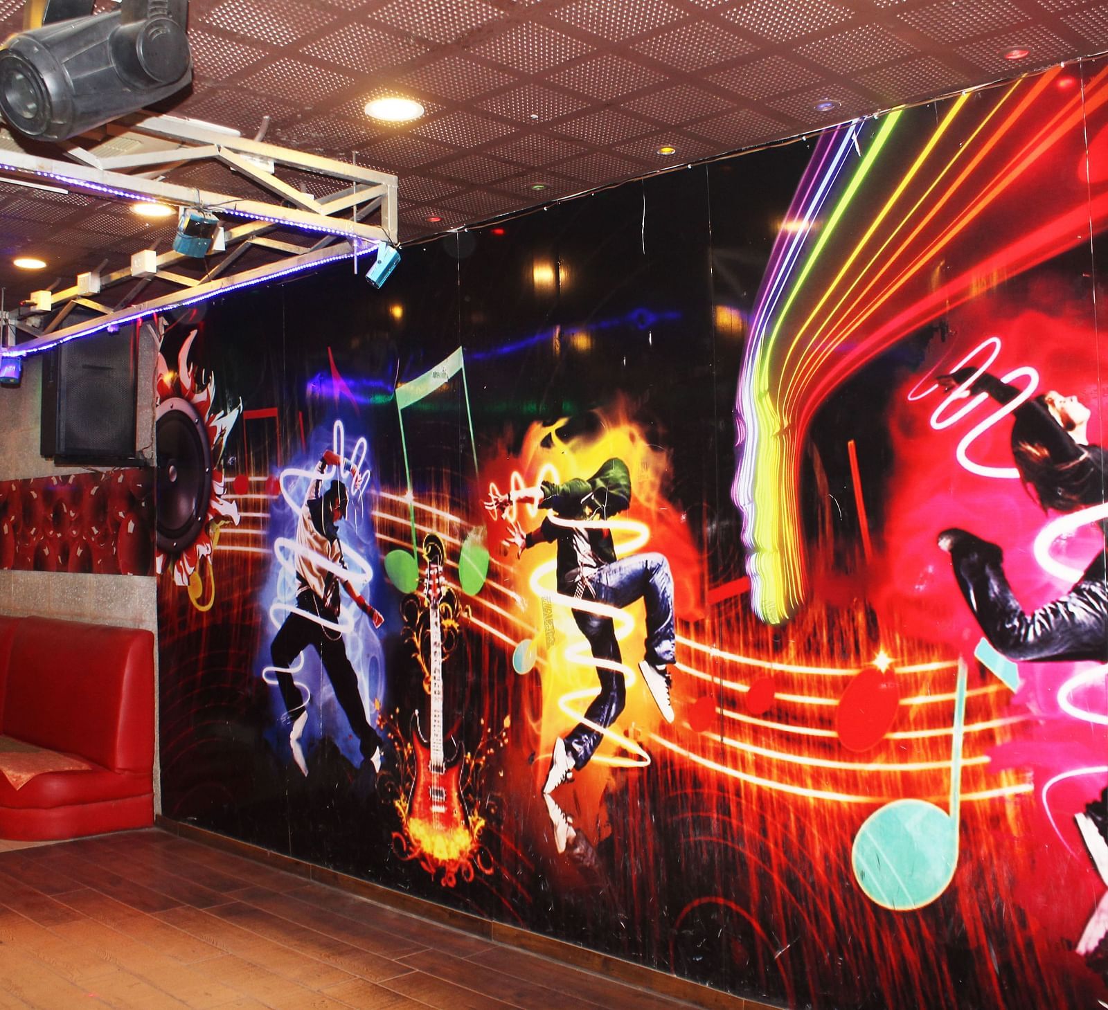 A dance club with vibrant wall murals of dancers, a red tufted sofa and disco lighting - TGI Apple Inn, Jaipur 