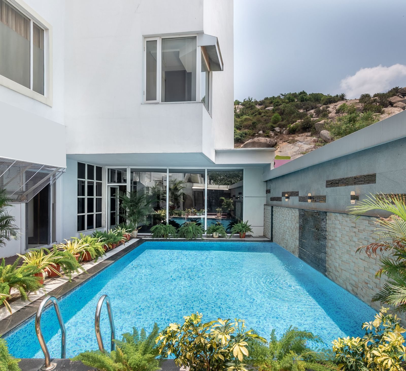 A swimming pool with clear water is surrounded by landscaping and a white building. The sky is overcast.