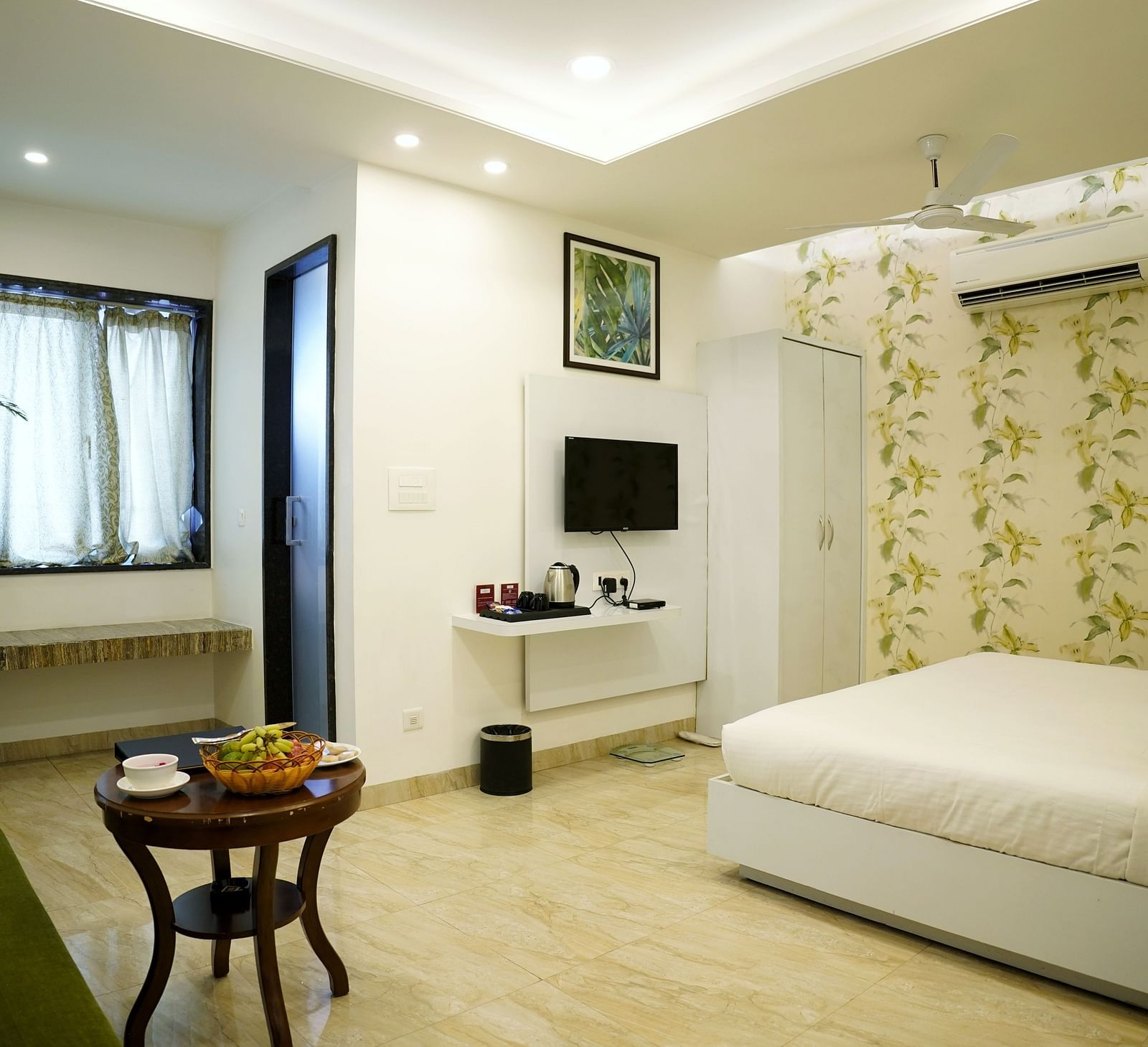 A serene bedroom setup with a large window and a white and green colour scheme - TGI Insignia, Bhopal