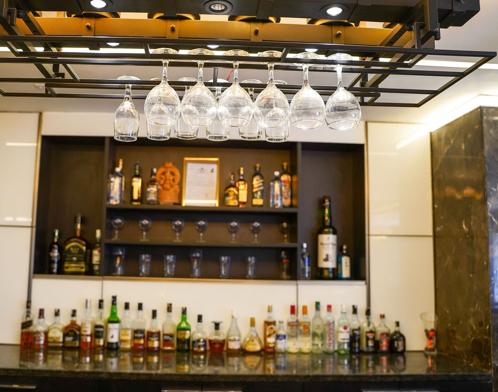  A well-stocked bar counter at BNGV Grandeur Hotel and Banquets, with various bottles of liquor and hanging glasses.