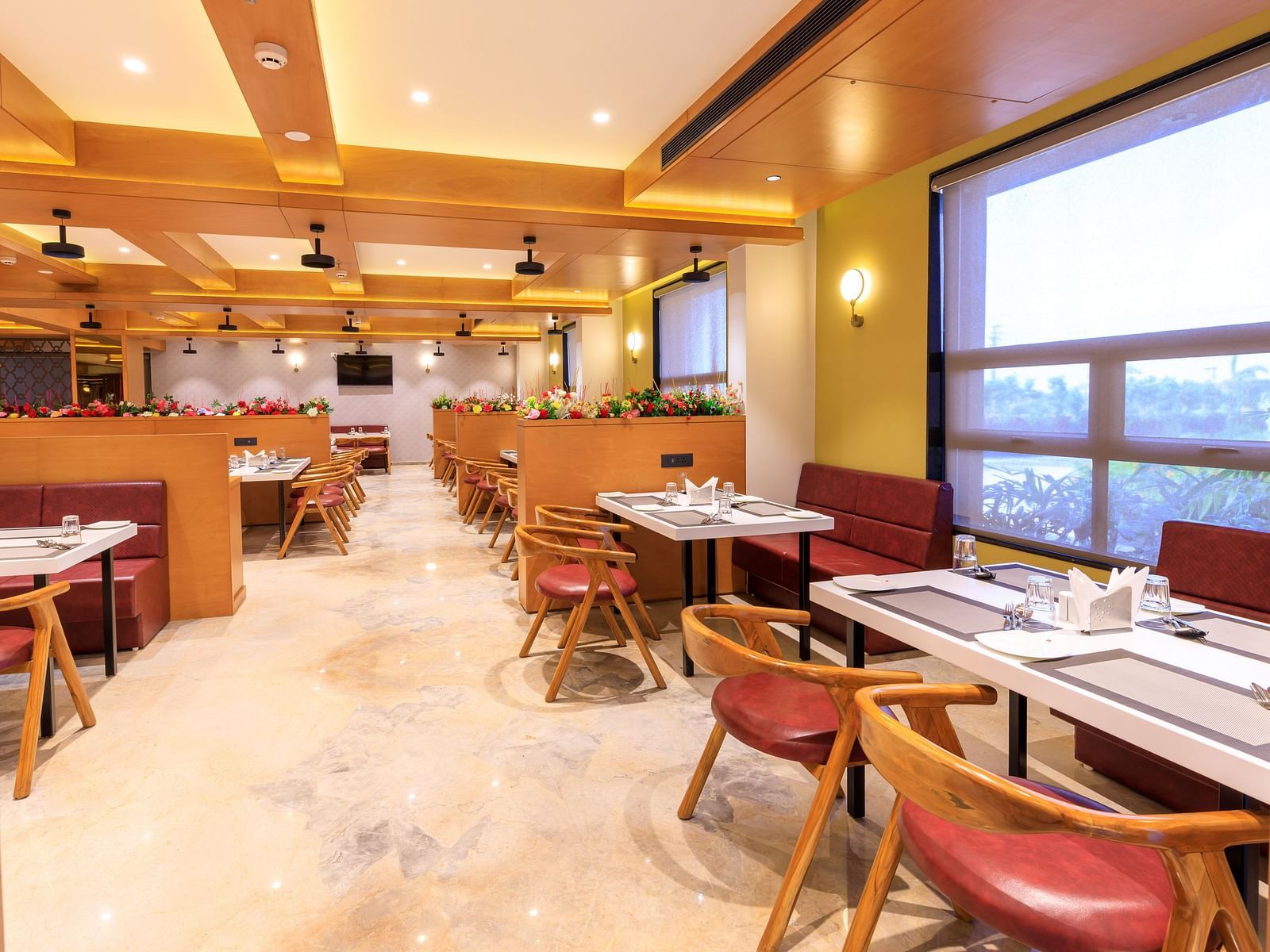 The brightly lit restaurant at Lords Eco Inn Apple Gate features set tables, red chairs, wooden accents, and natural light from large windows.