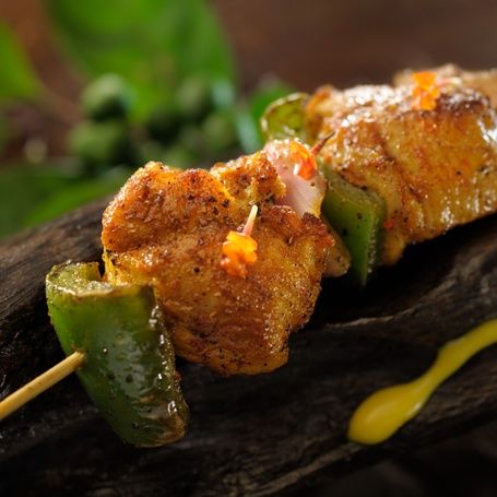 Grilled chicken and bell pepper skewers on wood.