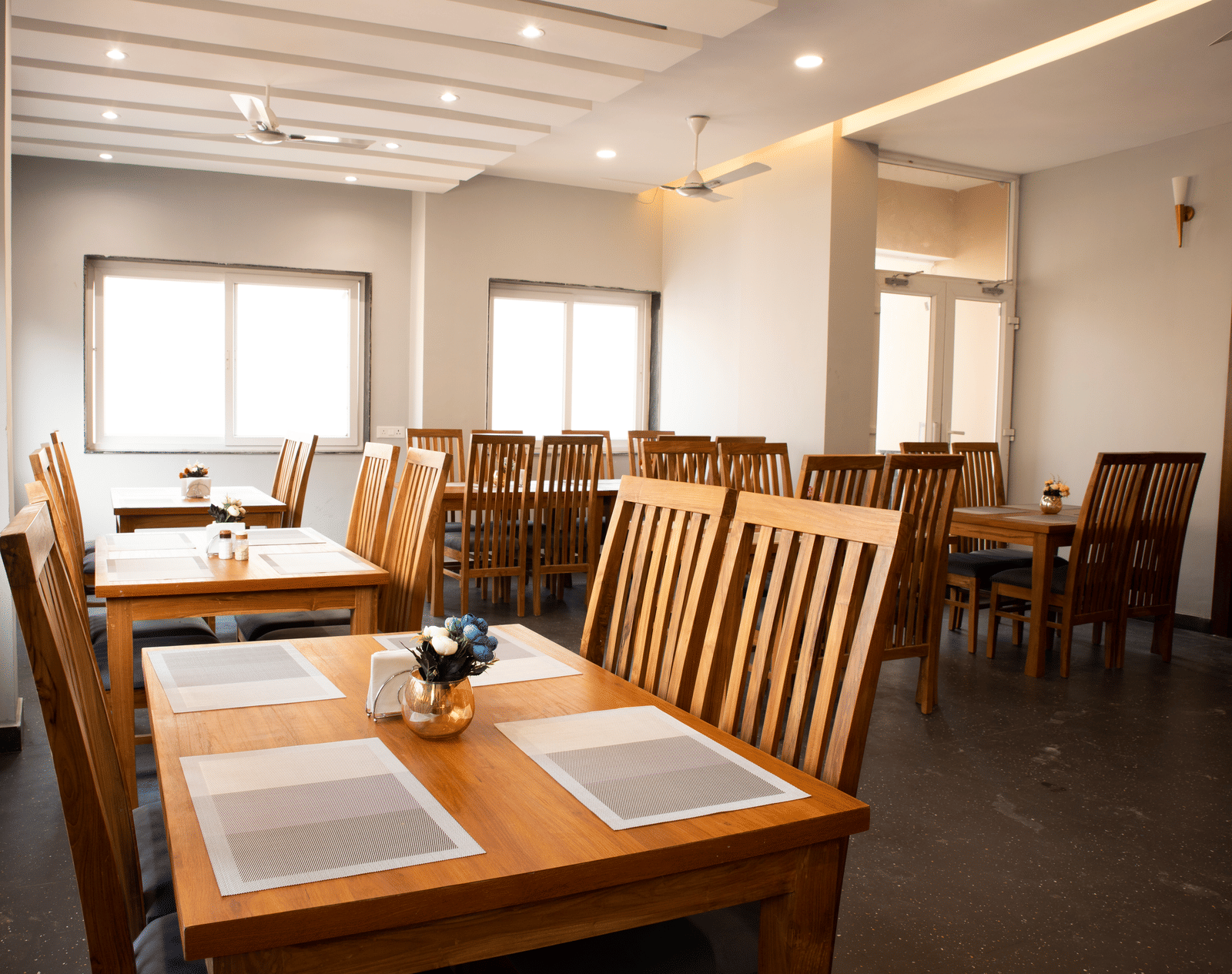 A dining area with wooden dining tables, place mats and chairs set neatly in a well-lit room at Perfectstayz Premium Laxmi Heritage, Rishikesh.