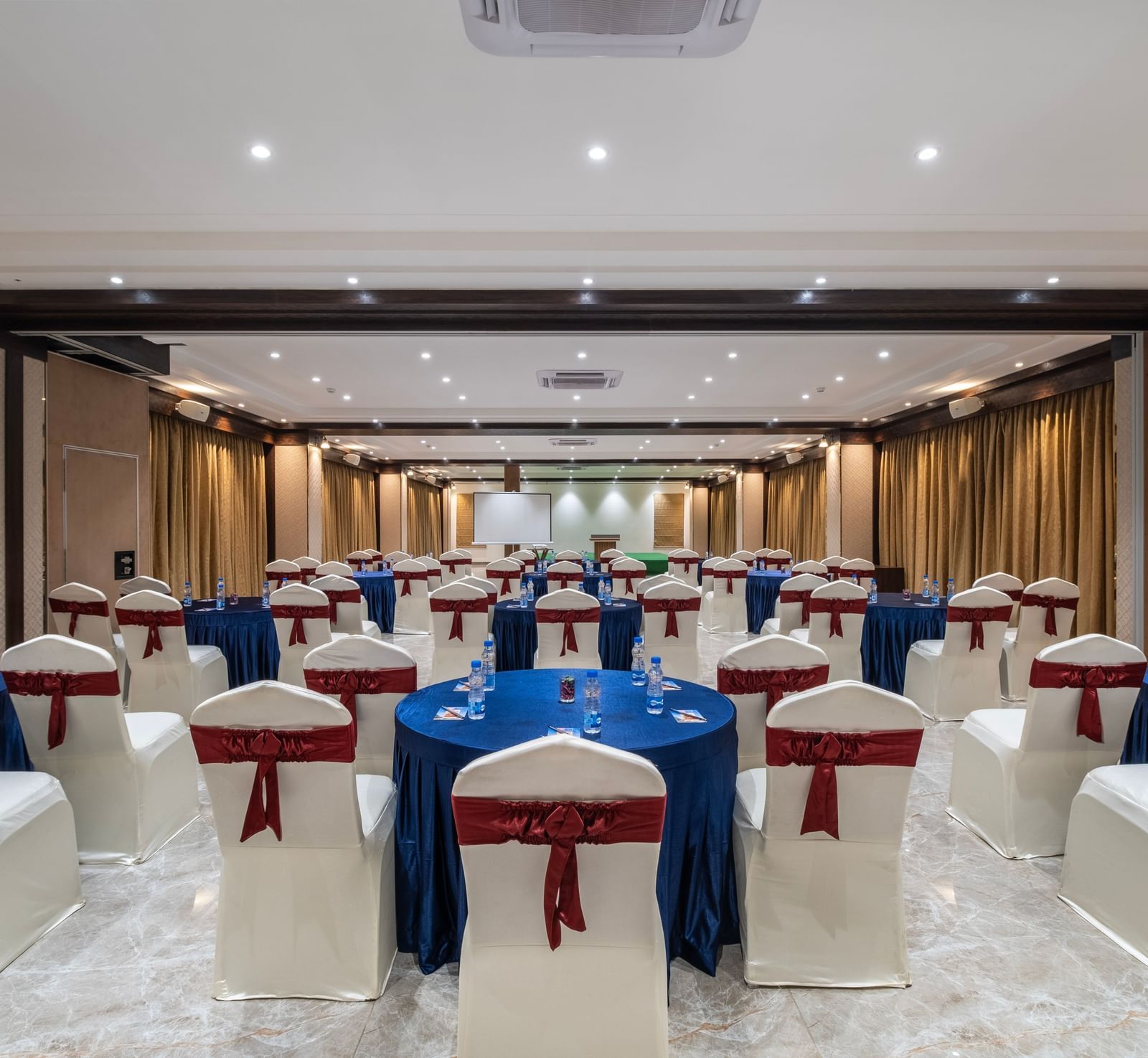 Back view of an event space at Monday Hotels Amalapuram Heights decorated with covered chairs.