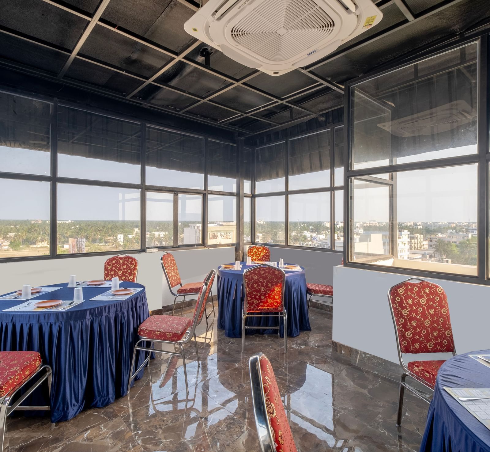 Glass-walled banquet area at Monday Hotels Amalapuram Heights with city view and cluster seating arrangement.