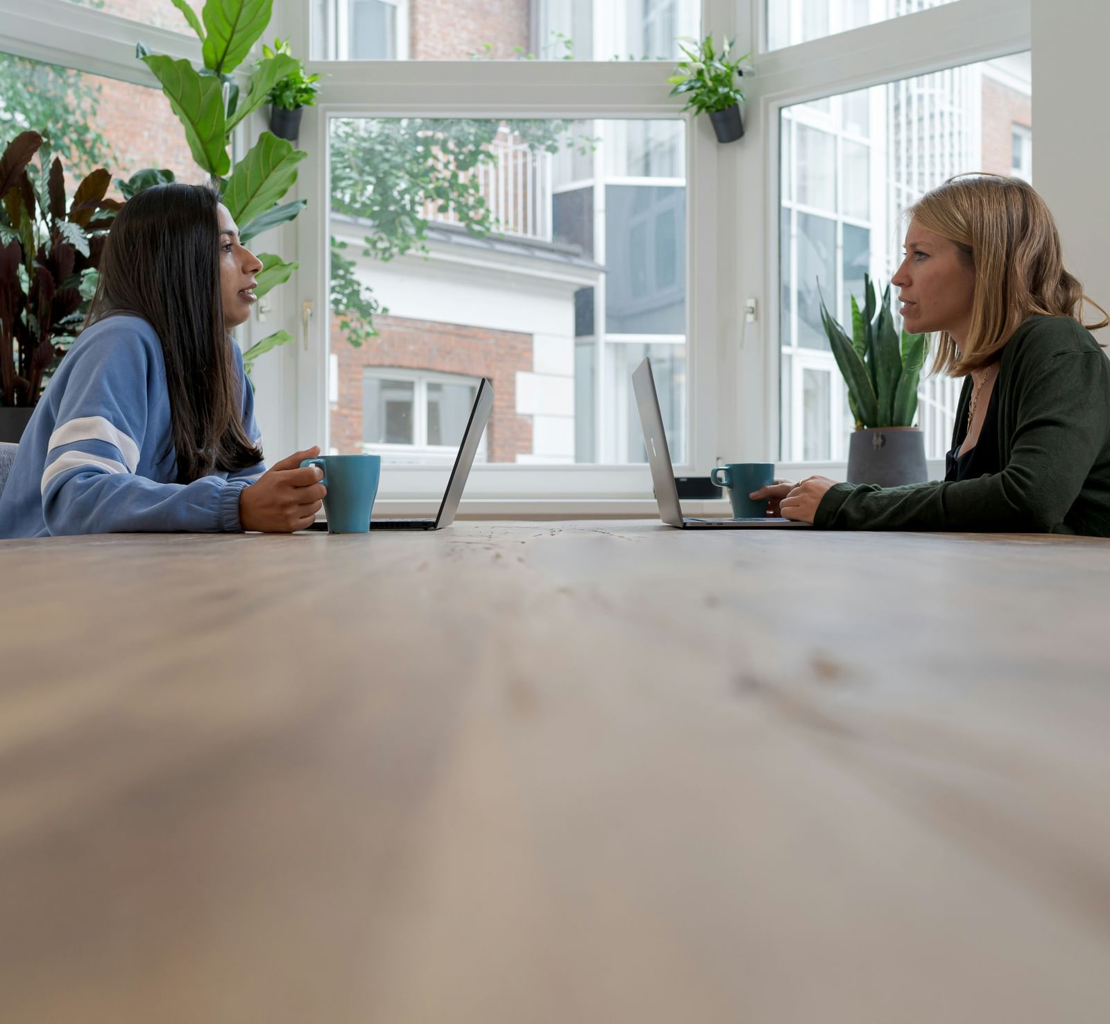 Two people in a conversation with each other placed on either sides of a wooden table.