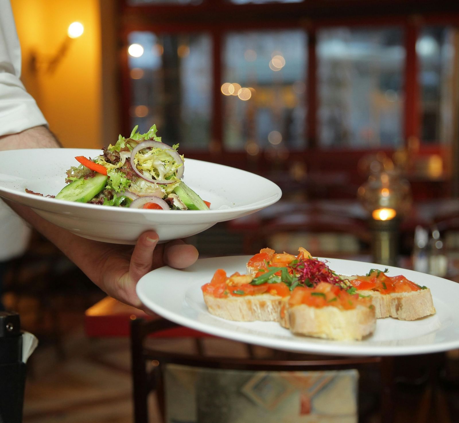 A person in a restaurant holding two plates with delicious dishes in it that are well plated.