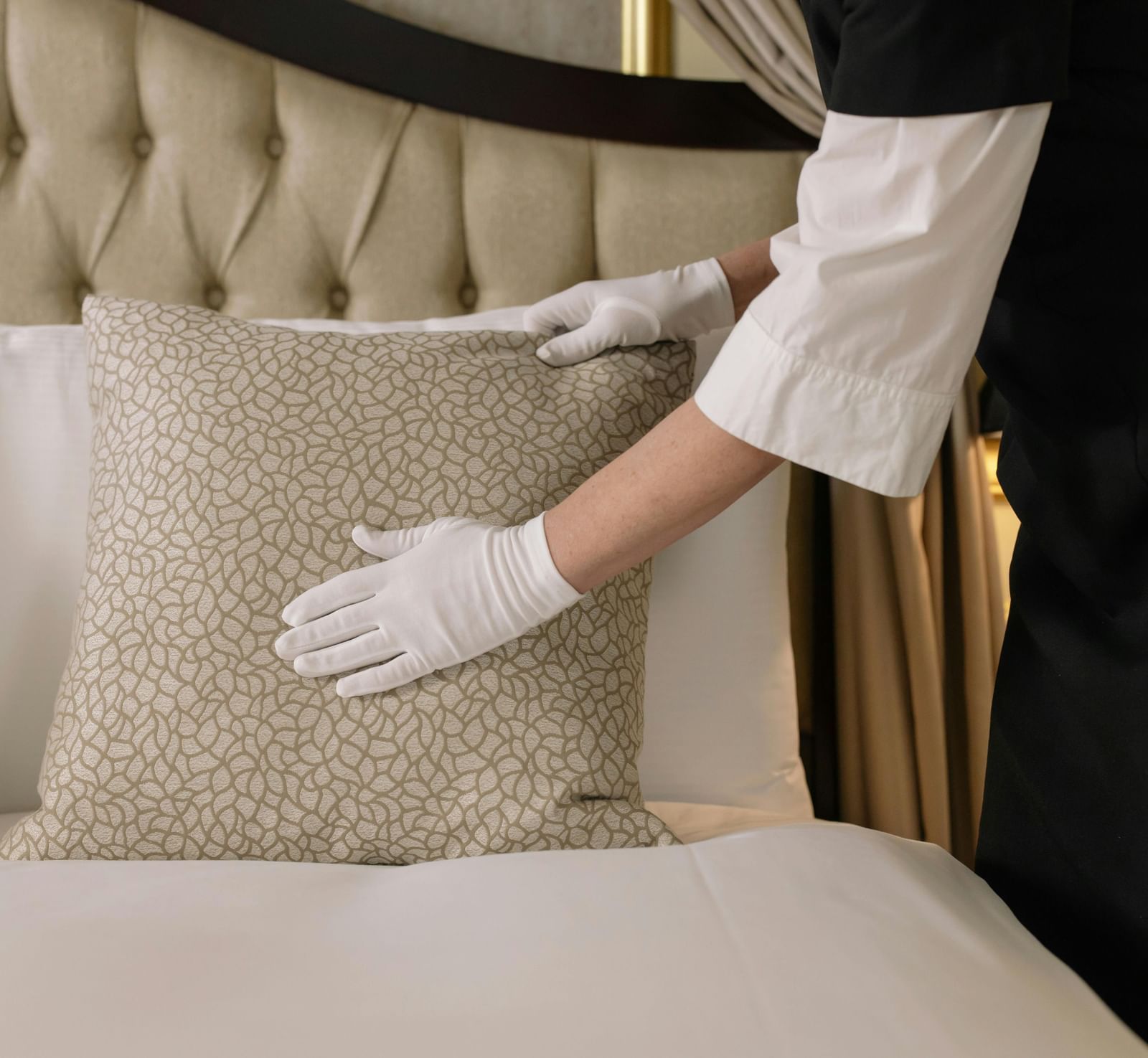 A housekeeper wearing white hand gloves making the bed at a hotel room.